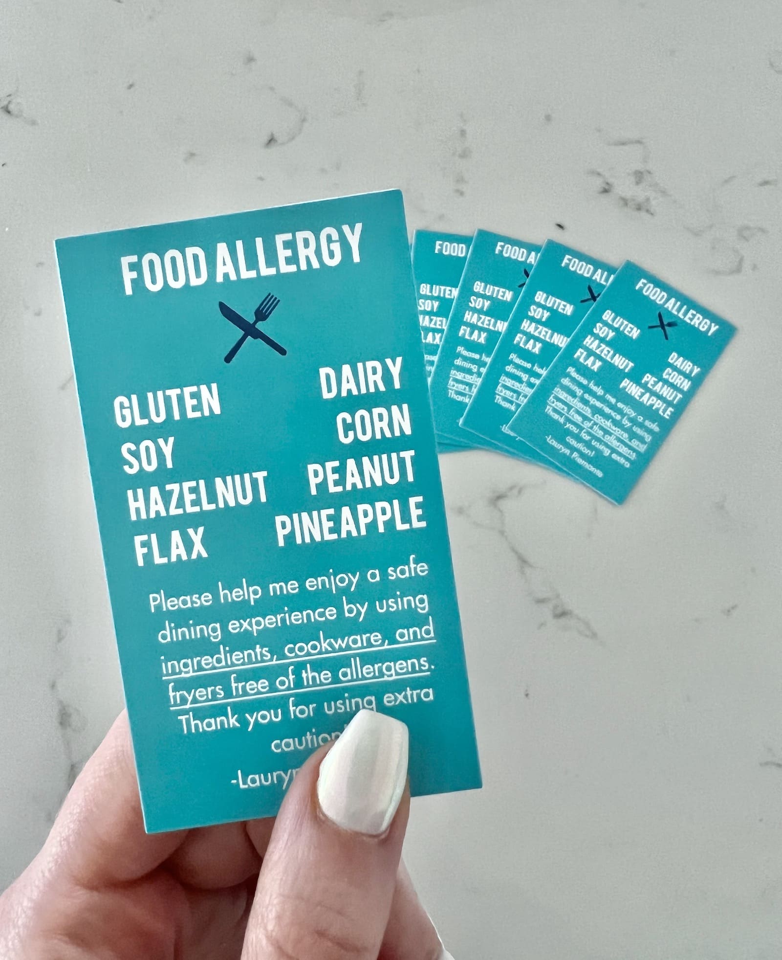 Holding a food allergy card for gluten, dairy, soy, corn, hazelnut, peanut, pineapple, and flax allergies.